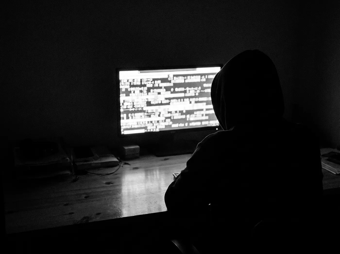 A hooded silhouette in front of a screen of scrambled characters